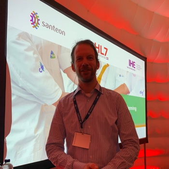 Bram Wesselo tijdens de presentatie op de Zorg&ICT beurs met op het scherm de logo's van Santeon, HL7 Nederland en IHE Nederland